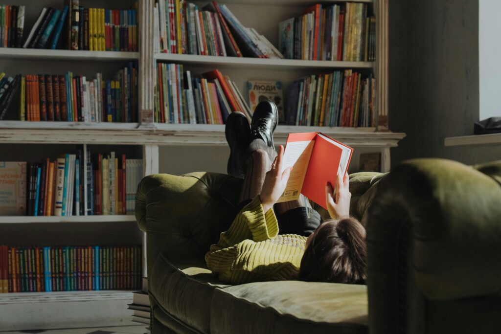 Young woman reading on a green sofa in a library, enjoying leisure time.